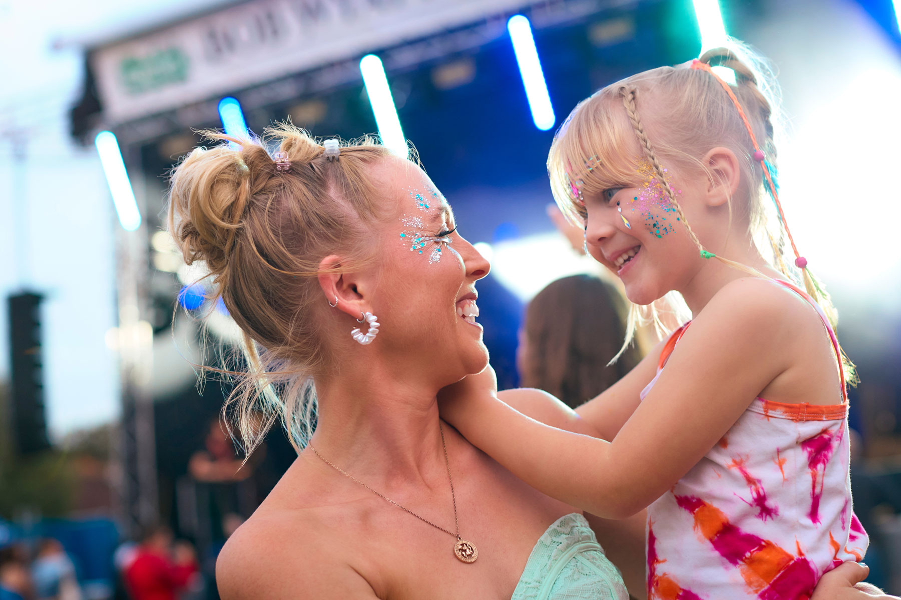 Mother With Daughter Wearing Glitter Having Fun At Outdoor Summer Music Festival